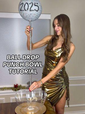 BALL DROP PUNCH BOWL TUTORIAL🪩 Ending the year with this DIY that turned out so cool! And if you’ve been around since Halloween, you know I love my dry ice🤪  🔗Shop the video on my LTK and Amazon. SUPPLIES: -Foam ball -Silver metallic spray paint -Glitter spray paint -Crafting paint -Soarkled -Mod podge -Paintbrush  -Wooden dowel -Black sparkly fabric -Hot glue gun -Punch bowl -Platter -Champagne glass -Punch or drink of choice -Ladle for serving  DIRECTIONS: 1. Spray paint your foam ball with silver metallic and glitter spray paint. 2. Paint on “2025.” 3. Add mod podge and sparkles on it. 4. Stick it through a wooden dowel. 5. Use hot glue to wrap some black sparkly fabric around the wood. 6. Hot glue punch bowl to platter. 7. Hot glue champagne glass in center of punch bowl. 8. Stick dowel in center of champagne glass and start adding your hot glue allllll around it. This takes a while but is so worth it! Once my champagne glass was completely doused with hot glue, I was able to prop mine up on the counter against a cabinet to let it dry for around an hour but the longer the better. 9. Add punch or drink of choice to your bowl and serve with a ladle! #balldrop #2025 #2025decor #nye #nyeparty #nyeideas #nyepunchbowl #nyefood #nyediy #newyear #newyearseve #newyearsparty #newyearsfood #newyearseveparty #newyearsevefood #newyearseveideas #newyearsideas #nye2025 #2025countdown 