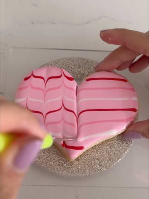 Try this fun wet-on-wet royal icing technique for an easy Valentine’s Day cookie design! ❣️Flood the base of your cookie and immediately add your colored stripes in the same flood consistency icing. Use a scribe tool or toothpick to drag your icing up and down, making sure to clean it off between each drag, working quickly before your icing dries 💗❤️ #cookies #cookiedecorating #sugarcookies #royalicing #royalicingcookies #baking #cookievideo #decoratedcookies #cookietutorial #cookiesoftiktok #ValentinesDay #tutorial 