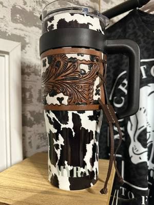 This Cowprint Tumbler is so cute!!! Loving the tooled leather sleeve that wraps it!  🥰🥰🥰🥰 #tumbler #westernfashion #cowprint #tooledleather #drinkinstyle #sippin 