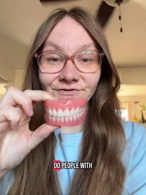 Do people with fake teeth brush? I will answer. Yes we do! We have to keep our dentures nice and clean.  Video Description: A toothless white lady with long brown hair, pink glasses and a blue shirt on. She is holding her dentures up and talking to the camera. #faketeeth #dentures #fyp 