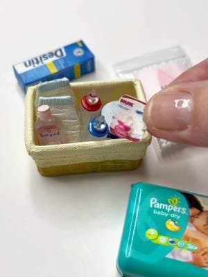 Can you spot all the baby essentials in this tiny basket? 🔍 Created this miniature nursery collection complete with all the newborn must-haves - from diapers to formula. Everything a baby needs, just teeny! 🧺✨ Miniature baby essentials arranged in a small woven basket. The items include tiny diapers, baby bottles and baby oil bottle by Re-Ment, Similac formula container by @Kim Davis Berry and a Nuk pacifier by @Geniesminihouseshop with a Pampers package from @AliExpress US  and Johnson’s cotton balls by @Sue's Mini Shop #miniatureworld #grandmagetsreal #miniatures #minithings #dollstagram #tinythings 