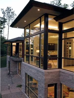 Expansive glass windows frame the breathtaking lake views, allowing natural light to flood the home and create a seamless connection with the outdoors With wooden exterior panels offering a rich, natural texture and carefully placed recessed lighting highlight the architectural features of this custom luxury home #exteriordesign #homeexterior #modernhome #luxuryhomes #luxuryliving #azdarchitects 